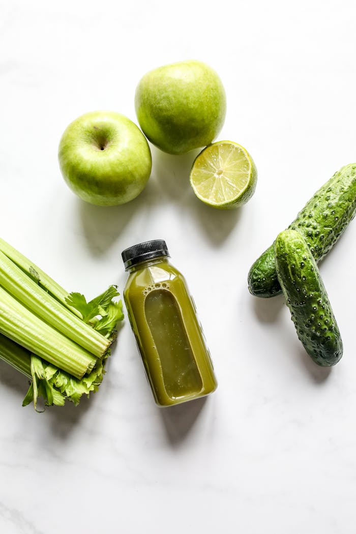 Top view of green smoothie ingredients including celery, cucumber, apple, and lime on white background.