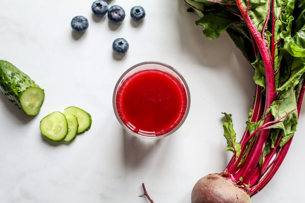 Top view of a vibrant beetroot juice with fresh cucumber and blueberries on a white background, perfect for a healthy lifestyle.